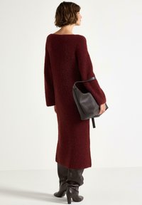 Bordeaux strikket kjole med lange ærmer, mid længde, struktureret stof, parret med en struktureret sort taske og knæhøje brune stiletter.
