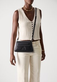 Black leather handbag with studded accents, featuring a structured shape and a long shoulder strap. The design includes a prominent logo.