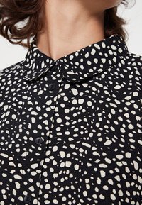 Black shirt with white irregular speckled pattern, featuring a button-down front and a rounded collar. Soft textured fabric.