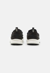 Scarpe sportive in suede nere con suole bianche, dotate di un upper testurizzato, tasselli per il trasporto e elementi di design minimalisti.