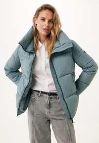 Jasnoniebieska kurtka puchowa z wysokim kołnierzem, suwakiem z przodu i detalami w prążki. Połączona z białą koszulą i szarymi dżinsami.