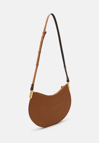 Brown leather shoulder bag with a curved shape, gold hardware, and an adjustable strap featuring black accents. Zipper closure on top.