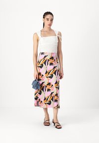 Vitt, strukturerat crop-top med justerbara band, parat med en lång, färgglad kjol med abstrakta blommönster i rosa, svart och orange.
