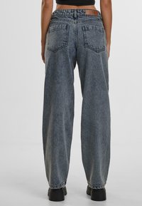 High-waisted, wide-leg denim jeans in faded blue with a smooth texture, featuring two back pockets and a contrasting brown leather patch.