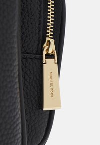 Pochette con zip in pelle nera opaca con hardware dorato, caratterizzata da un'etichetta rettangolare incisa con "MICHAEL KORS".