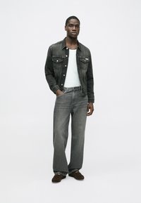Sort denimjakke over en hvid skjorte, kombineret med grå viddejeans og mørkebrune sko. Outfittet har en moderne pasform og klassisk design.