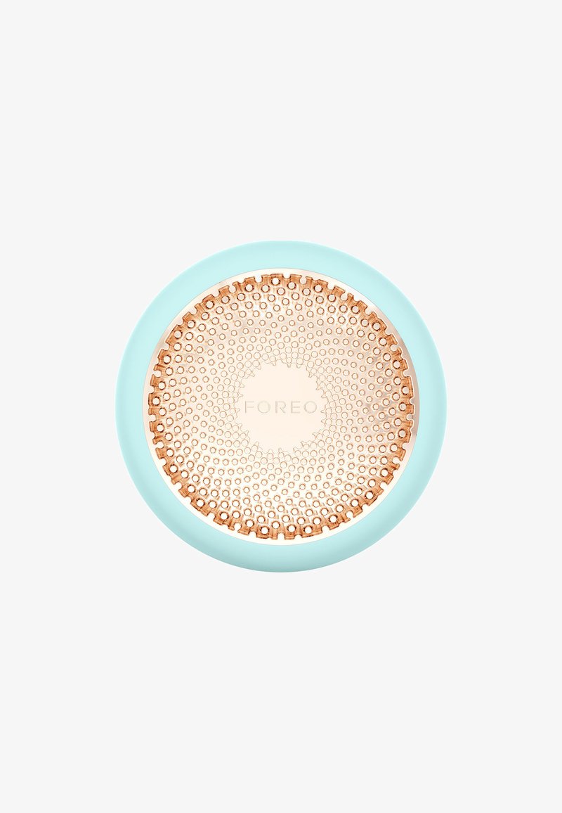 Round facial cleansing device in light blue silicone with a textured rose gold surface, featuring circular patterns and a central logo.