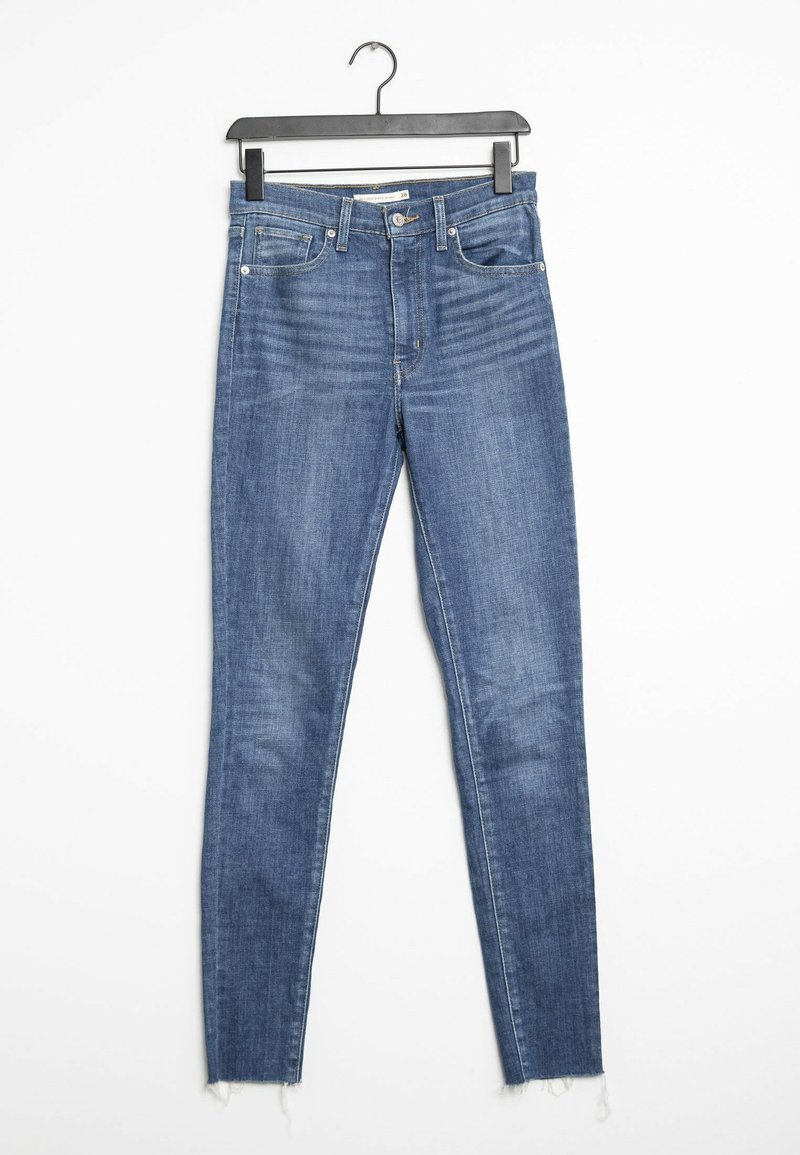 Jean skinny bleu en denim avec une taille mi-haute, présentant des déchirures minimales et des ourlets effilochés. Design classique à cinq poches et quincaillerie en métal.