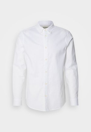 Chemise blanche à manches longues en coton, dotée d'un col structuré, d'une broderie de logo discrète et de boutons beige clair.