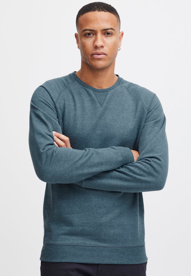 Sudadera de color teal oscuro hecha de tela suave. Presenta un escote redondo, puños acanalados y un diseño simple sin patrones ni logotipos visibles.