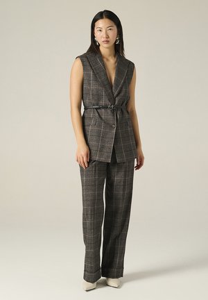 Blazer senza maniche grigio a quadri con scollatura a V profonda, abbinato a pantaloni larghi coordinati. Cintura nera che stringe in vita. Tessuto con texture liscia.