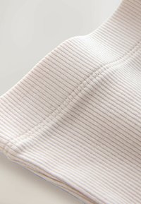 Rippstoff in zartem Beige mit subtilen hellbraunen Streifen. Glatte Textur mit sichtbaren Nähten entlang der Kanten und Nähte.