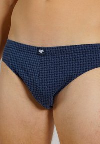 Marineblauwe slips met een houndstooth-patroon, gemaakt van zachte stof, met een logo op de tailleband en een aansluitend ontwerp.