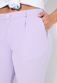 Licht lavendelkleurige broek gemaakt van een gladde stof, met een voorzak, een vlakke voorkant en een knoopsluiting met dubbele stiksels.