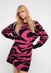 Πλεκτό φόρεμα σε μαύρο με έντονες ροζ ρίγες ζέβρας. Διαθέτει μακριά μανίκια και στρογγυλή λαιμόκοψη. Μαλακή υφή με άνετη εφαρμογή.
