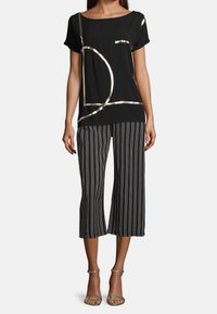 Top corto nero con maniche corte e motivi geometrici dorati, abbinato a culotte a righe bianche e nere. Sandali dorati completano l'outfit.