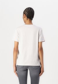 Lys beige bomulds t-shirt med korte ærmer, en rund halsudskæring og en lige pasform. Bæres med grå jeans. Simpelt design, ingen synlige mønstre eller accenter.