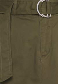 Tessuto verde oliva con una texture liscia, caratterizzato da una cintura larga con una fibbia rotonda in argento e cuciture a contrasto lungo le cuciture.