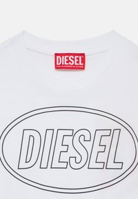 Λευκό βαμβακερό t-shirt με μεγάλο μαύρο οβάλ σχήμα και το κείμενο «DIESEL» στο κέντρο. Κόκκινη ετικέτα ραμμένη στο λαιμό με την επιγραφή «FOR SUCCESSFUL LIVING.»