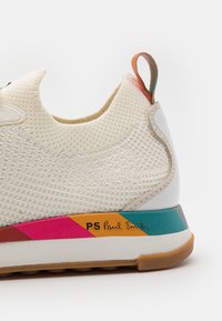 Bílé síťované tenisky s vícebarevným pruhem na podrážce, s texturovaným povrchem a poutkem na patě.