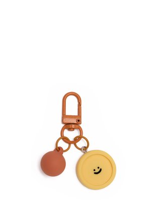 Porte-clés avec un fermoir marron attaché à deux anneaux, tenant une sphère marron et un pendentif circulaire jaune avec un visage souriant noir.