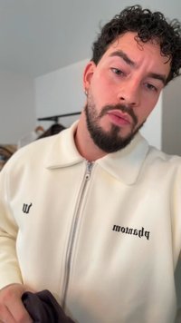 Giacca bianca con cerniera a costine e colletto, con testo stampato in nero sul petto sinistro e una persona che tiene un oggetto scuro.