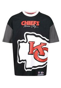 Sort og hvid t-shirt med teksten "CHIEFS Kansas City", stort rødt "KC" logo og et geometrisk design med grå accenter. 100% bomuldsstof.