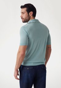 Gaiši zils polo krekls ar īsām piedurknēm, ribinātu apkakli un apakšmali. Valkāts ar tumšu džinsu biksēm, kurām ir aizmugurējās kabatas un pogu detaļa.