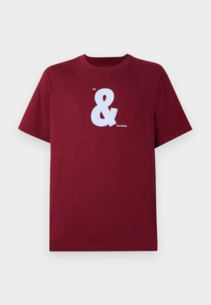 T-shirt curta marrom com um grande ampersand branco e pequeno texto "me" e "my calvins" no centro da frente.