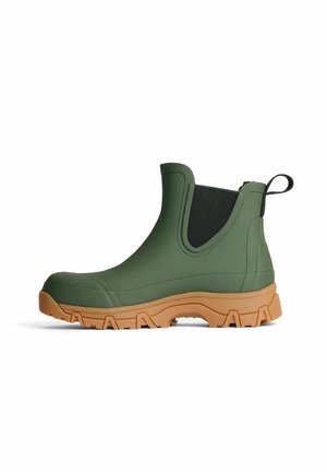 Grüner knöchelhoher Gummistiefel mit schwarzen elastischen Seitenteilen und dicker beiger Profilsohle, von der Seite vor weißem Hintergrund betrachtet.