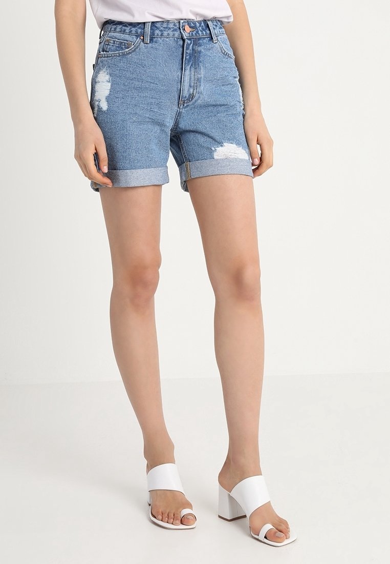 Džínové kraťasy světle modré barvy s opraným designem, s ohrnutými manžetami a předními kapsami. Nosené s bílými sandály na vysokém podpatku.