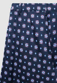 Jupe fluide bleu marine avec un motif floral rouge et bleu, comportant des formes de diamant, des plis et une taille avec passants de ceinture. Texture lisse.