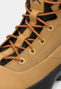 Stivale da trekking in pelle color cuoio con mesh nero, lacci a contrasto rossi e gialli, occhielli dorati e suola in gomma nera con grip testurizzato.