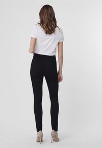 High-waisted black denim jeans with a fitted design and two back pockets, paired with a plain white t-shirt and beige heels.