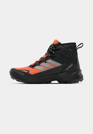 Black and orange hiking boot with a textured upper, prominent lacing system, silver accents, and a rugged sole for traction.