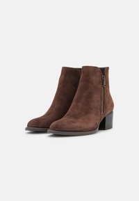 Bottes chelsea en suédine marron avec un bout arrondi et une fermeture éclair sur le côté, présentant un talon bloc robuste et une texture lisse.