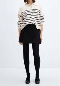 Pull en tricot avec une base crème et des rayures bleu marine, associé à une jupe plissée noire et des collants noirs. Chaussures : ballerines noires.