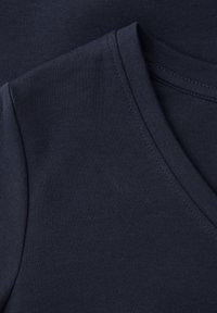 Gros plan sur un t-shirt bleu marine foncé à col en V montrant le col, la couture de l'épaule et la texture du tissu en maille fine.