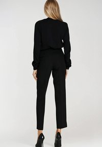 Czarny top z długim rękawem o luźnym kroju, połączony z dopasowanymi czarnymi spodniami. Wysokie obcasy dopełniają wygląd, podkreślając elegancką sylwetkę.