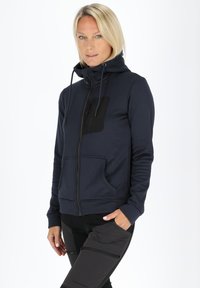 Navy zip-up hoodie with high collar, black front pocket, and adjustable drawstrings. Features kangaroo pocket and ribbed cuffs. Smooth texture.