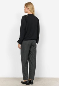 Černá halenka s dlouhým rukávem a texturovanými ramenními detaily, kombinovaná se šedými kalhotami s pruhy. Černé boty na blokovém podpatku. Minimalistický design.