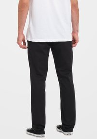 Pantaloni neri a gamba dritta realizzati in cotone con una texture liscia, abbinati a sneakers bianche; la camicia è una semplice T-shirt bianca.
