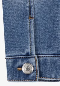 Mörkblå denimmanschett med kontrasterande gyllene stygn och en silvermetalldekor. Tyget har en strukturerad väv som är typisk för denim.