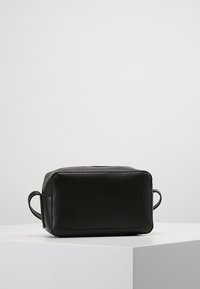 Černý kožený kosmetický pytlík s obdélníkovým tvarem, zipovým uzávěrem a bočními madly. Má hladký povrch a jemný embosovaný detail na přední straně.