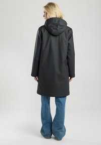 Zwarte waterdichte jas met capuchon, middellange ontwerp, gladde textuur, lange mouwen en geen zichtbare sluitingen, gedragen over lichtblauwe flared jeans.
