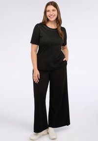 Top negro de canalé con mangas cortas y escote redondo, combinado con pantalones negros de pierna ancha. La modelo lleva zapatillas blancas. Diseño simple y elegante.