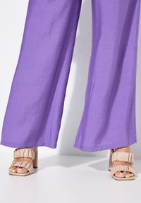 Paarse wijde broek van lichtgewicht stof, gecombineerd met beige chunky-heeled sandalen met gehoste banden.