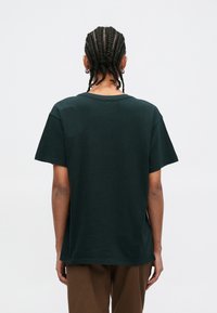 T-shirt en coton vert foncé, coupe décontractée, manches courtes et col rond, avec une texture lisse et un ourlet droit.