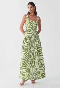 Robe maxi rayée verte et blanche avec un décolleté carré, taille élastique et tissu fluide et léger. Comprend des poches et une coupe décontractée.