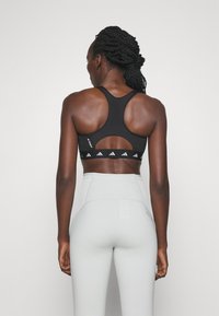 Sostenedor deportivo negro con un diseño de espalda nadadora y detalle recortado; cuenta con una banda elástica blanca con la marca. Combinado con leggins gris claro de cintura alta.